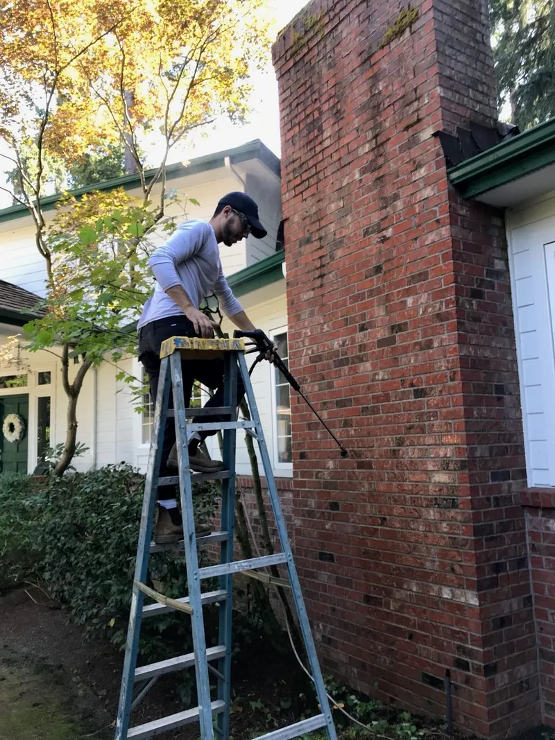 Chimney technician on ladder repointing mortar joints on brick chimney exterior