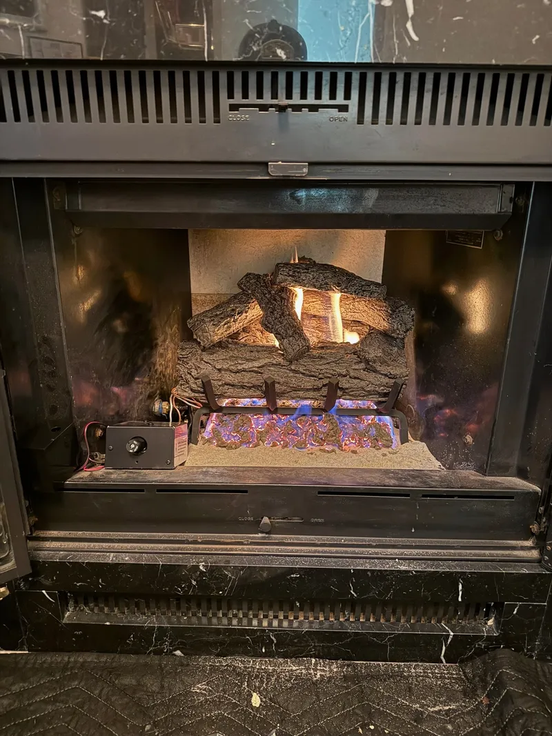 Gas log set installed in a dark marble masonry fireplace