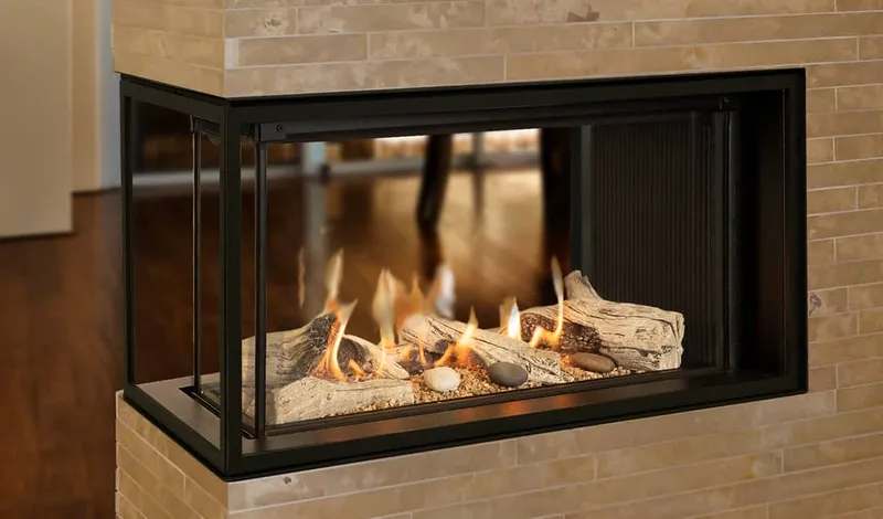 Valor three-sided see-through gas fireplace with driftwood logs and river stones in a travertine tile surround